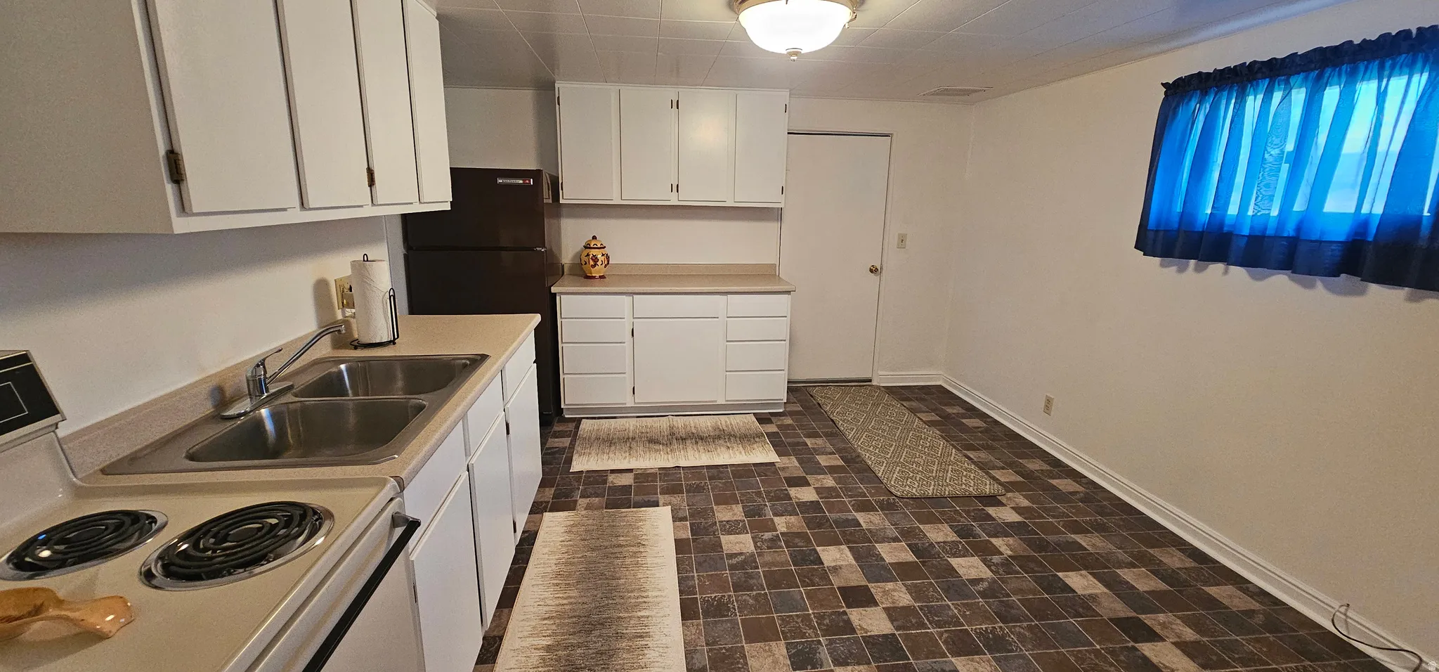 Kitchen featuring white cabinetry, light-toned countertops, a double basin stainless steel sink, and patterned flooring