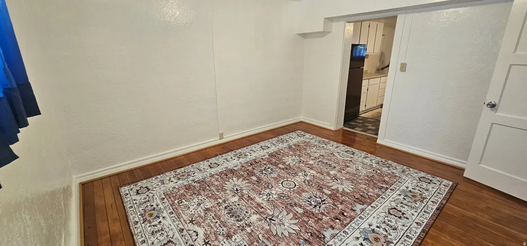 Hardwood flooring with a decorative area rug, white painted walls, and white baseboards