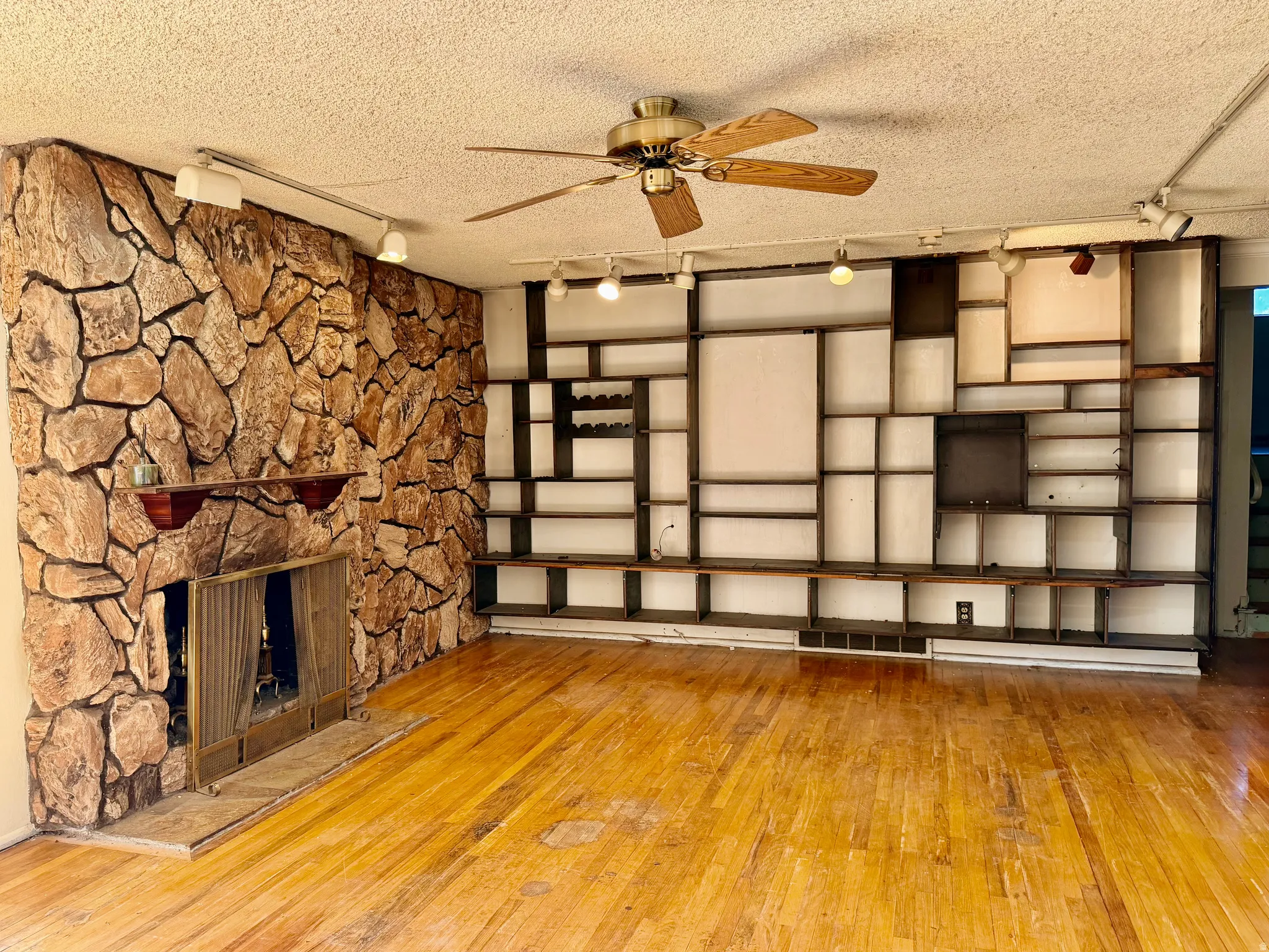 Spacious living area featuring wood flooring, a stone-clad fireplace with mantel, and a multi-level built-in shelving system