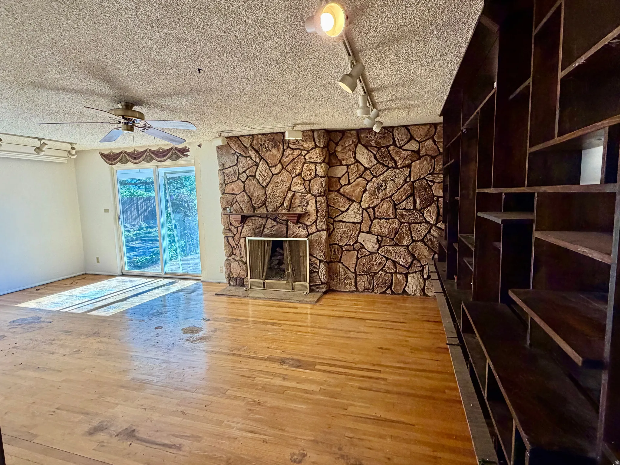 Stone-faced fireplace with a mantel, built-in shelving, wood  flooring