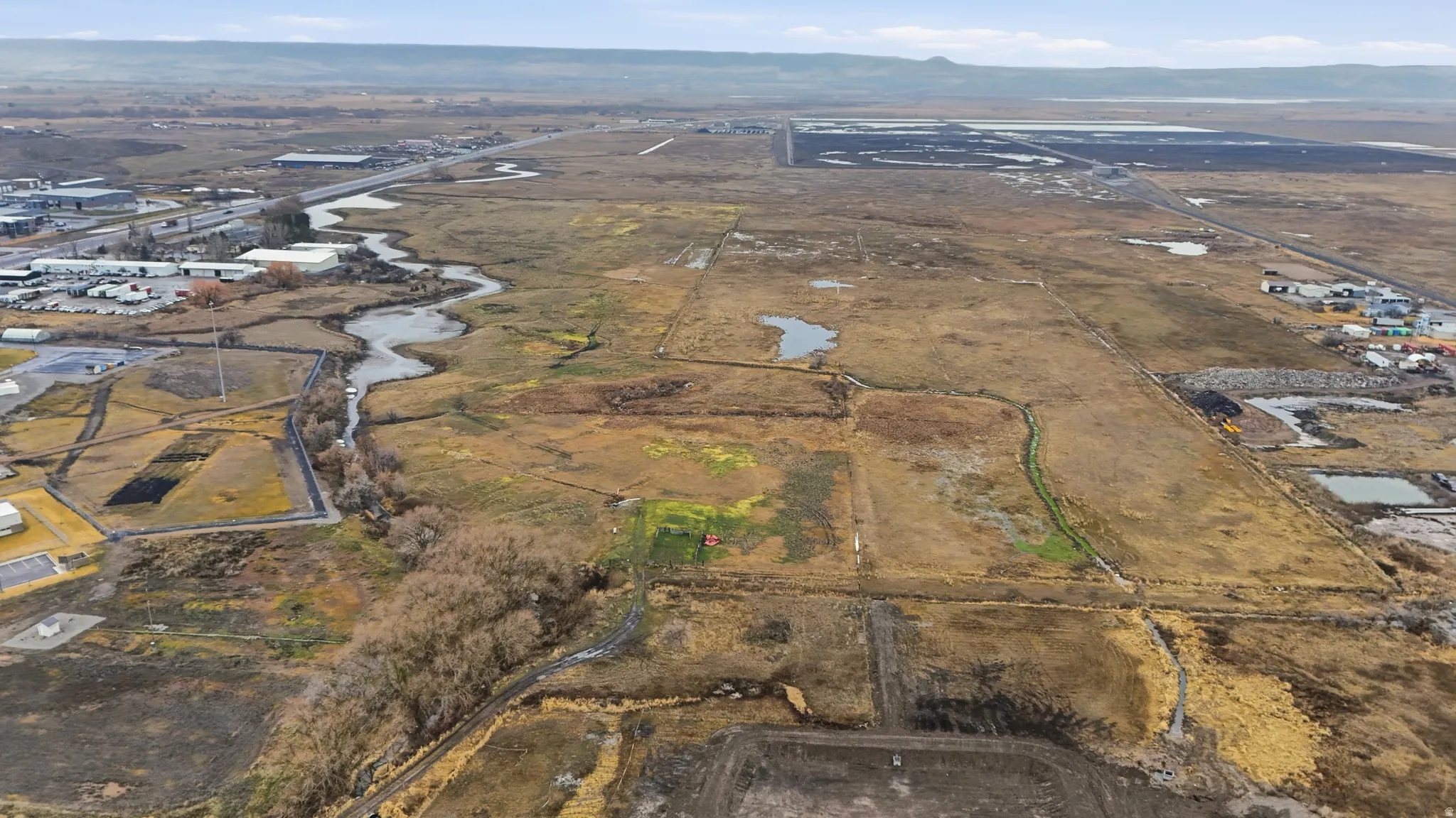 Expansive aerial parcel featuring varied terrain, a winding natural waterway, and distant infrastructure