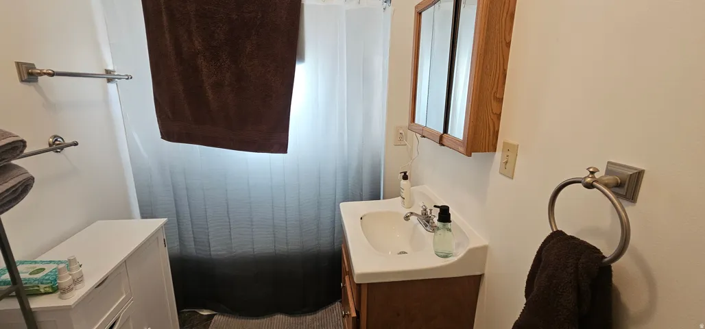 Bathroom featuring a white ceramic sink with chrome fixtures, a wood-finish vanity, and a mirrored medicine cabinet