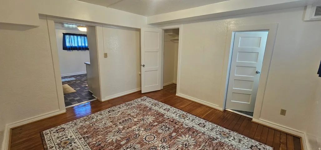 Wood-finish flooring throughout, featuring a traditional paneled door, a recessed closet with built-in shelving, and a doorway to an adjoining area with tiled flooring