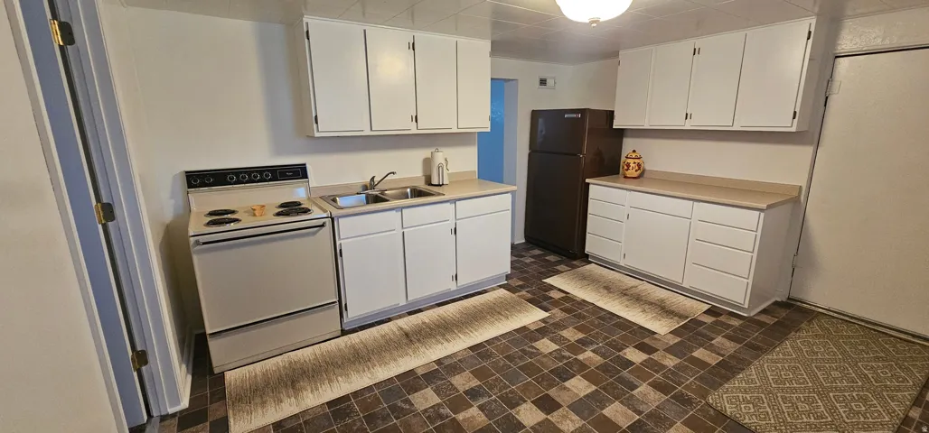 Kitchen featuring white cabinetry, a dual-basin stainless steel sink, a freestanding range, a refrigerator, and a checkerboard-patterned floor