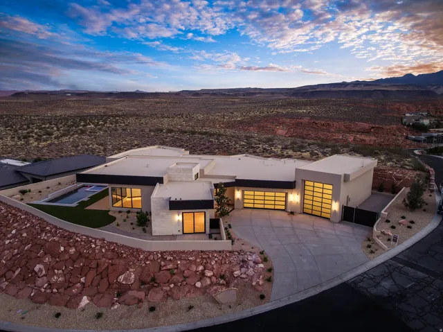 Modern desert-style residence featuring a flat roofline, an integrated swimming pool, and a paved driveway leading to translucent garage doors