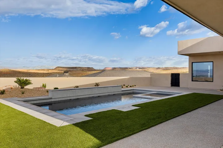 Expansive outdoor living area featuring a rectangular pool with an integrated spa, a water feature, artificial turf sections, and a surrounding concrete patio