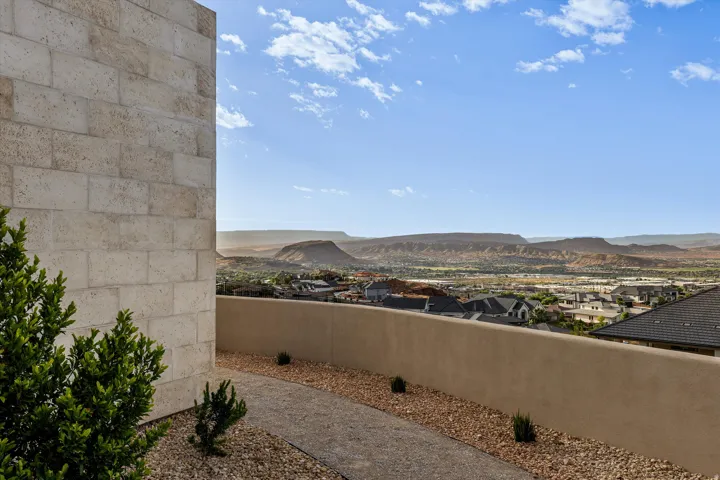Stone-clad exterior wall with a xeriscaped pathway, low-maintenance plantings, and a stucco retaining wall