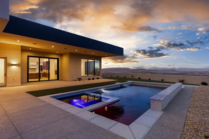 Modern rear exterior with expansive concrete patio, multi-level pool with integrated spa, arid landscaping, and broad sliding glass doors