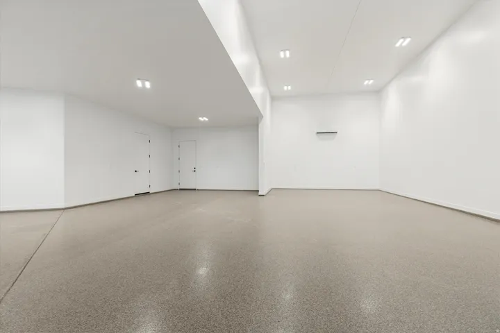 Spacious interior space featuring a durable epoxy floor finish, recessed ceiling lighting, clean white walls, and a wall-mounted climate control unit