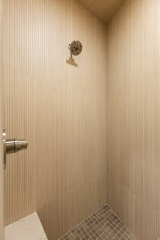 Shower enclosure featuring textured wall tiles, a rainfall showerhead, and a tiled floor