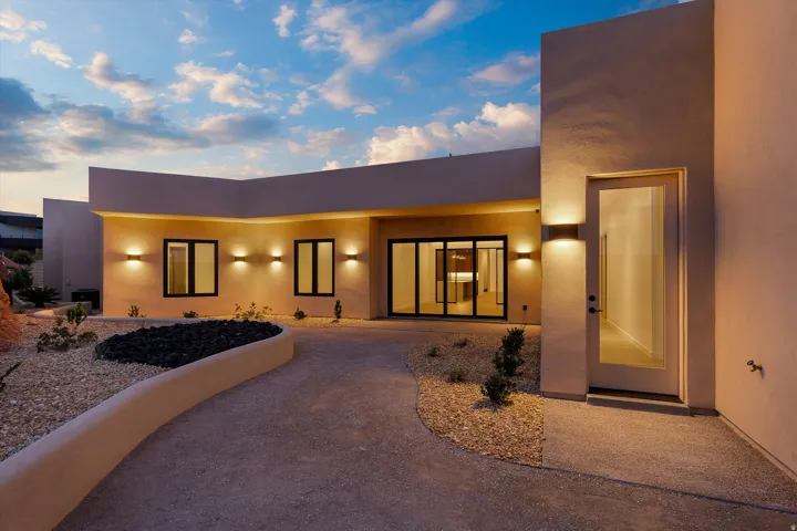 Contemporary stucco exterior featuring a glass-paneled entry door, multiple dark-framed windows, and integrated exterior lighting