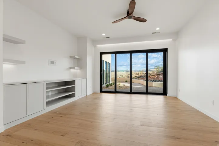 Expansive room featuring light wood-finish flooring, a contemporary ceiling fan, and built-in cabinetry with open shelving