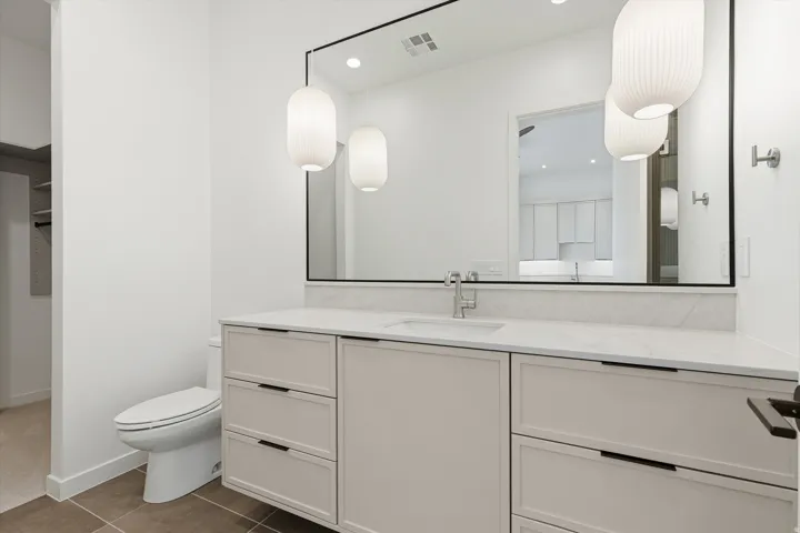 Bathroom featuring a dual-basin vanity with a white countertop and integrated sinks, under-mount cabinetry, and a full-width mirror with two pendant light fixtures