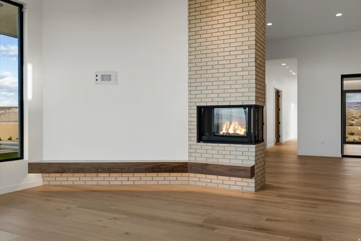 Central brick fireplace with a three-sided firebox, integrated wood-finish mantel, and light wood-finish flooring