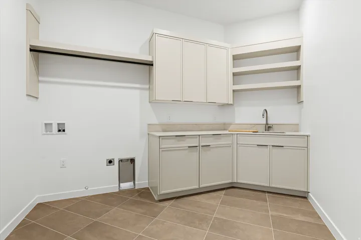 Utility room with tile flooring, built-in cabinetry, solid surface countertops, a utility sink with a gooseneck faucet, and integrated open shelving