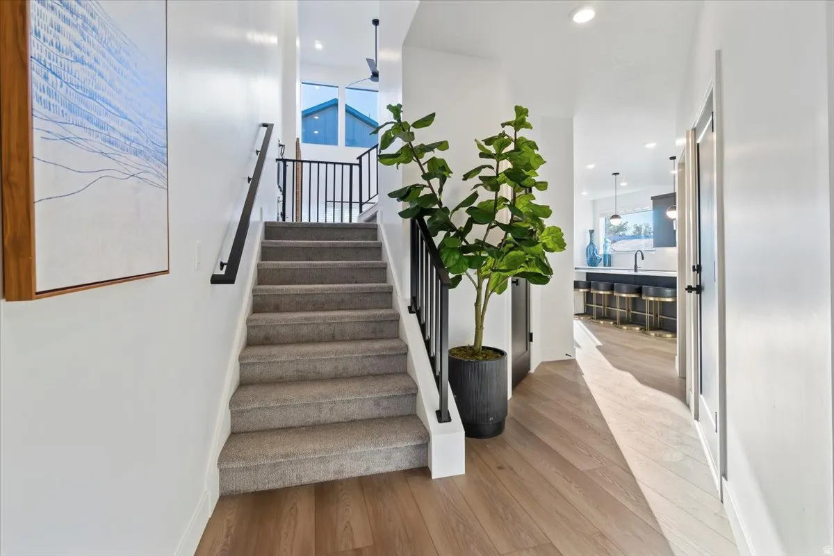 Carpeted staircase with black iron railing, wood-finish flooring, recessed lighting, and a modern kitchen with dark cabinetry and pendant lighting