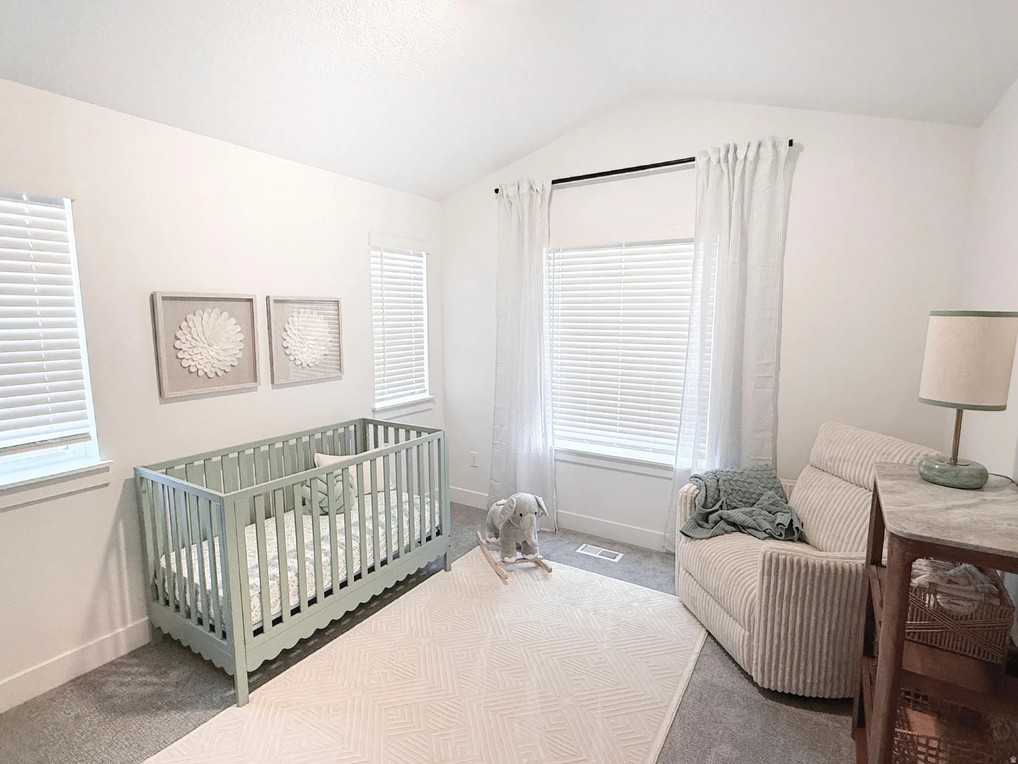 Vaulted ceiling accentuates this room featuring multiple windows with blinds and white drapes, and plush carpeting