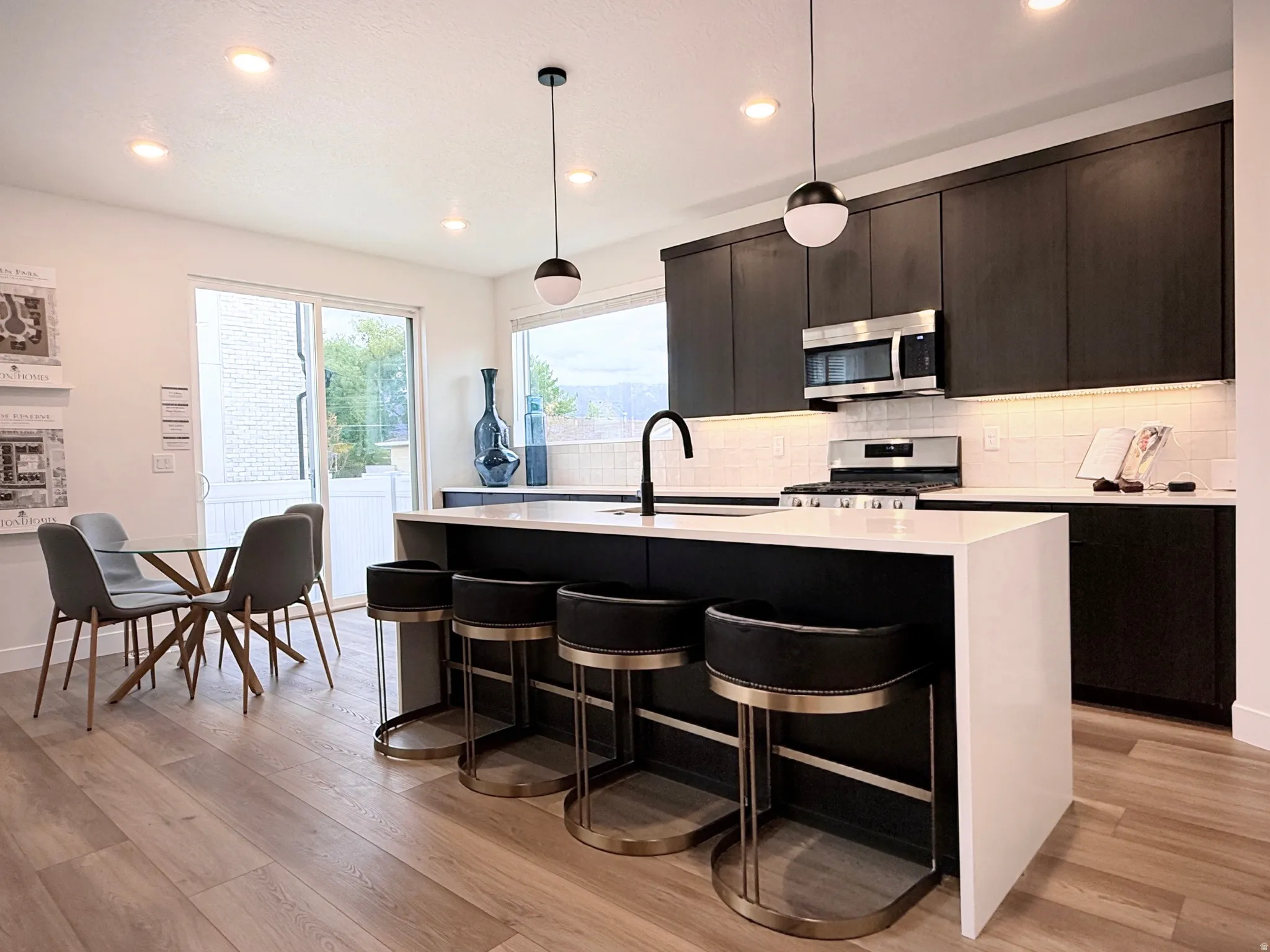 Modern kitchen featuring dark cabinetry, stainless steel appliances, a white subway tile backsplash, and a large island with white countertops