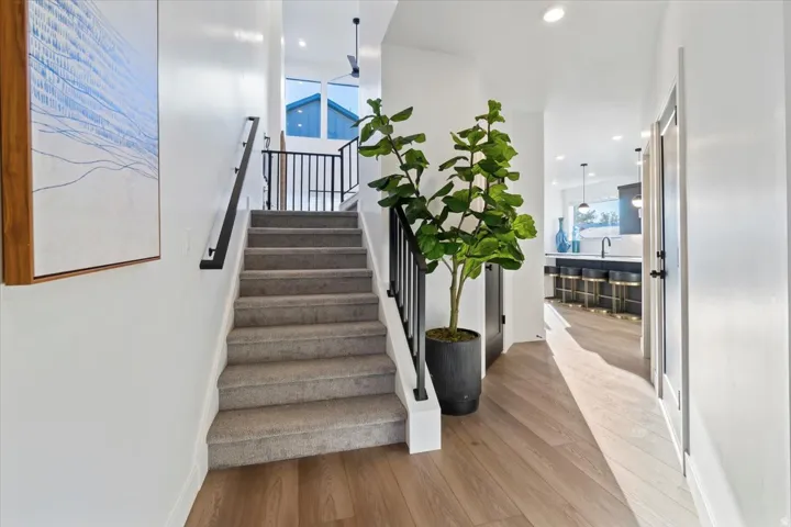 Carpeted staircase with black iron railing, wood-finish flooring, recessed lighting, and a modern kitchen with dark cabinetry and pendant lighting