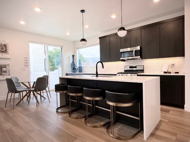 Modern kitchen featuring dark cabinetry, stainless steel appliances, a white subway tile backsplash, and a large island with white countertops