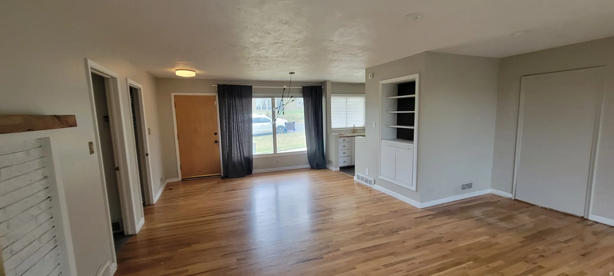 Open concept living area featuring wood-finish flooring, a contemporary chandelier, a built-in shelving unit, and a fireplace with a wood mantel