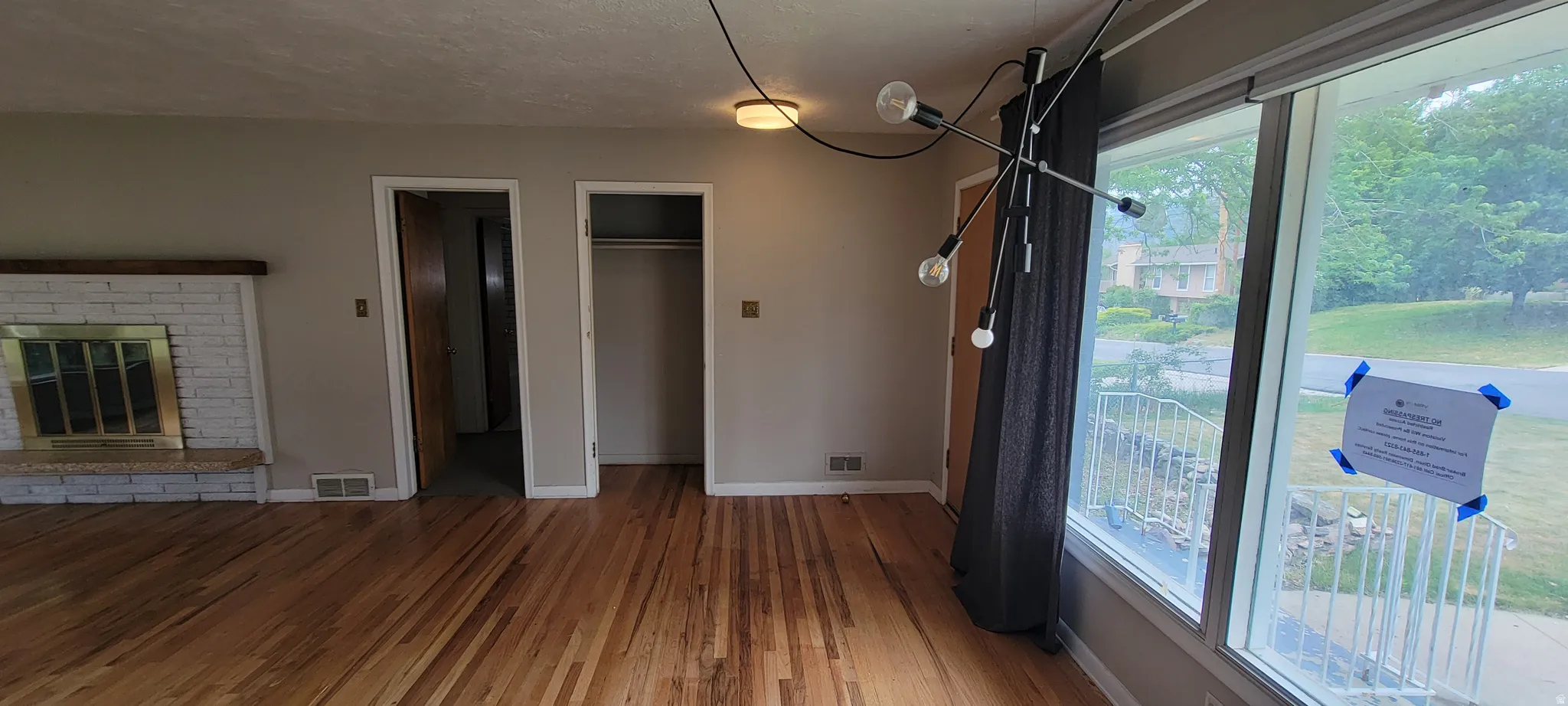 Hardwood flooring throughout featuring a white painted brick fireplace with a stone hearth