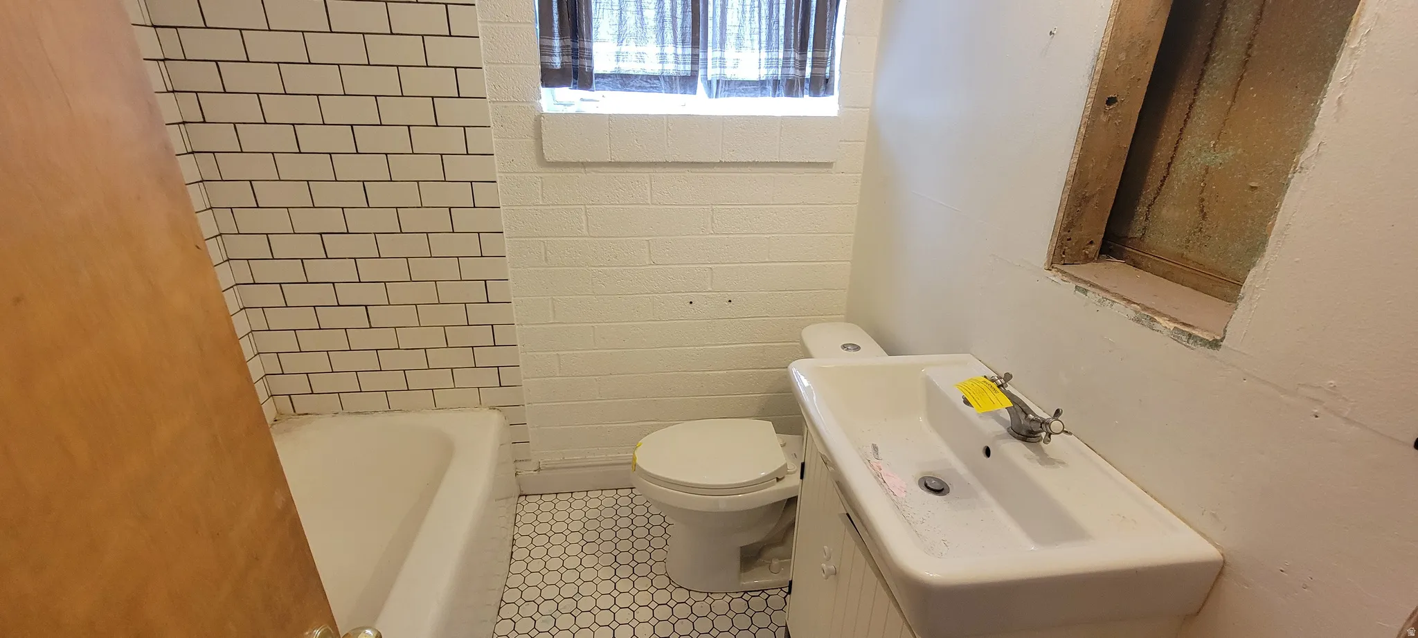Bathroom featuring white subway tile surround, white bathtub, white toilet, vanity with integrated white sink, and white hex mosaic floor tile