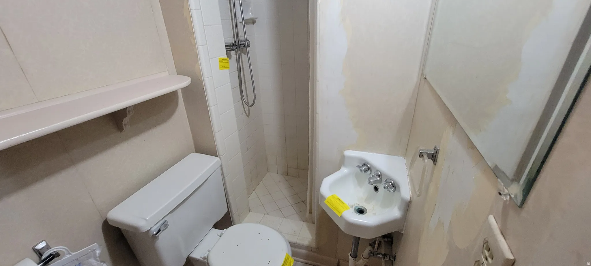 Compact bathroom featuring a corner pedestal sink with chrome fixtures, a white toilet, and a tiled shower stall