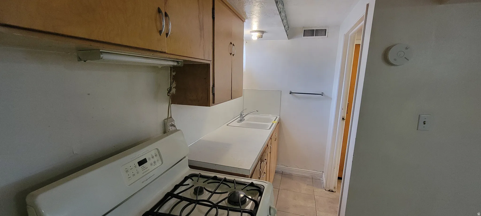 Kitchen area featuring a gas range, dual basin sink, wood cabinetry, and laminate countertops