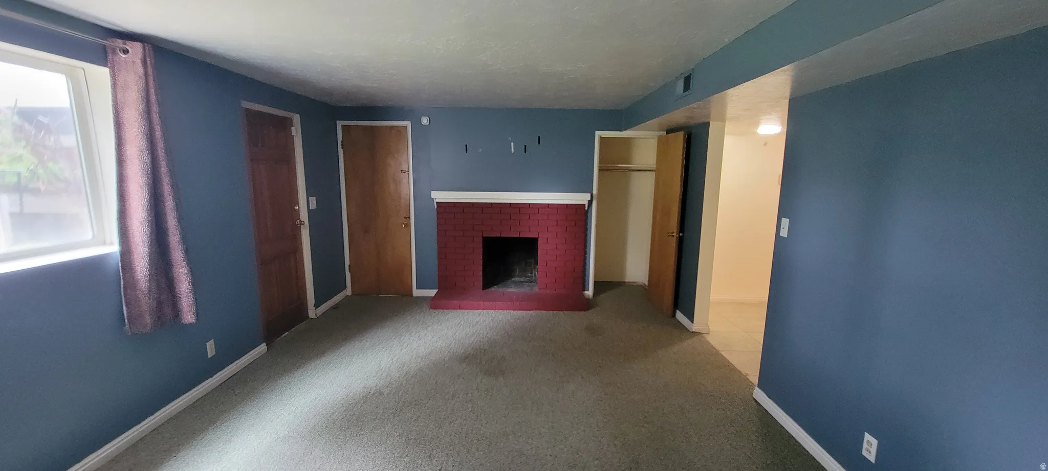 Interior space featuring a red brick fireplace with a white mantel, blue wall paint, and light-colored carpeting