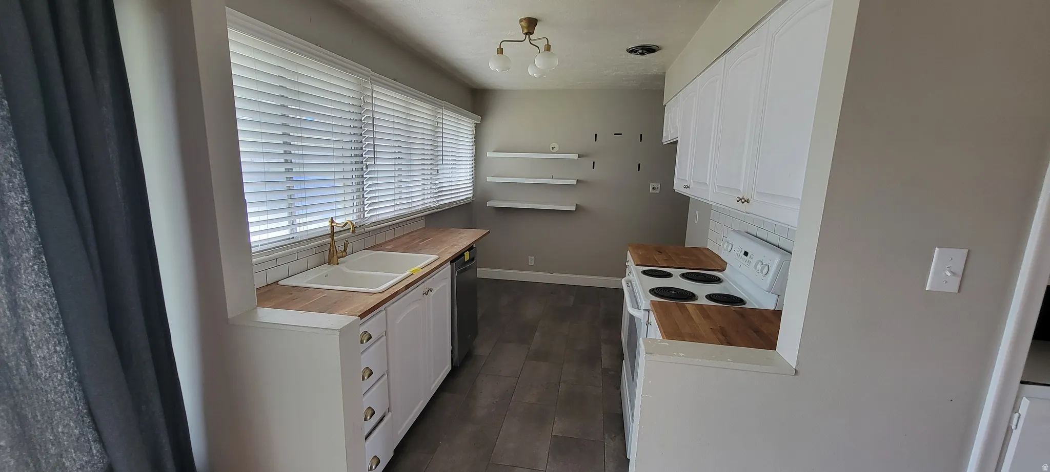 Kitchen featuring white cabinetry, wood-finish countertops, a dual basin sink with a brass-tone faucet, and a white tile backsplash