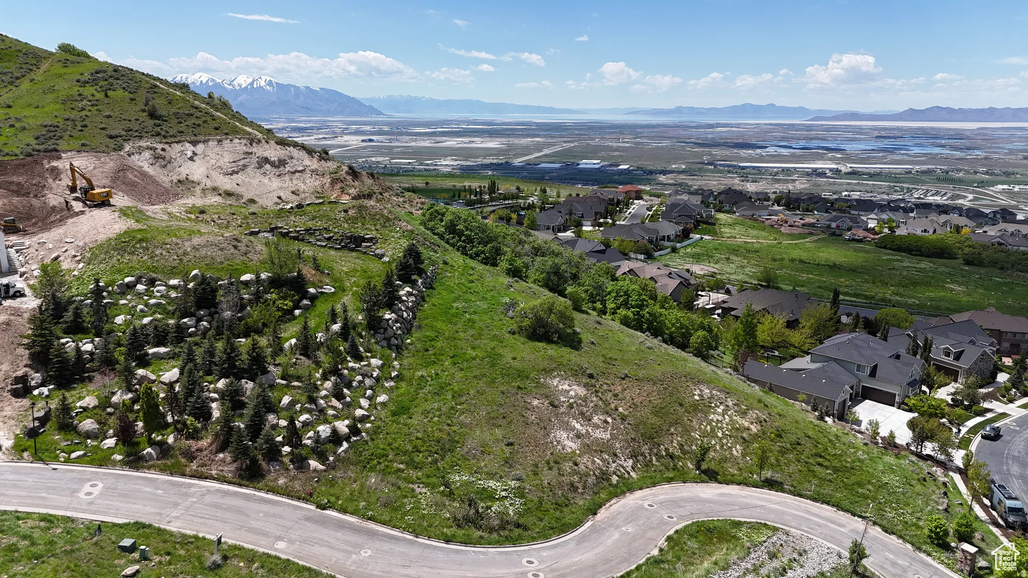 Expansive elevated lot with a paved road, natural rock formations, and mature evergreen trees