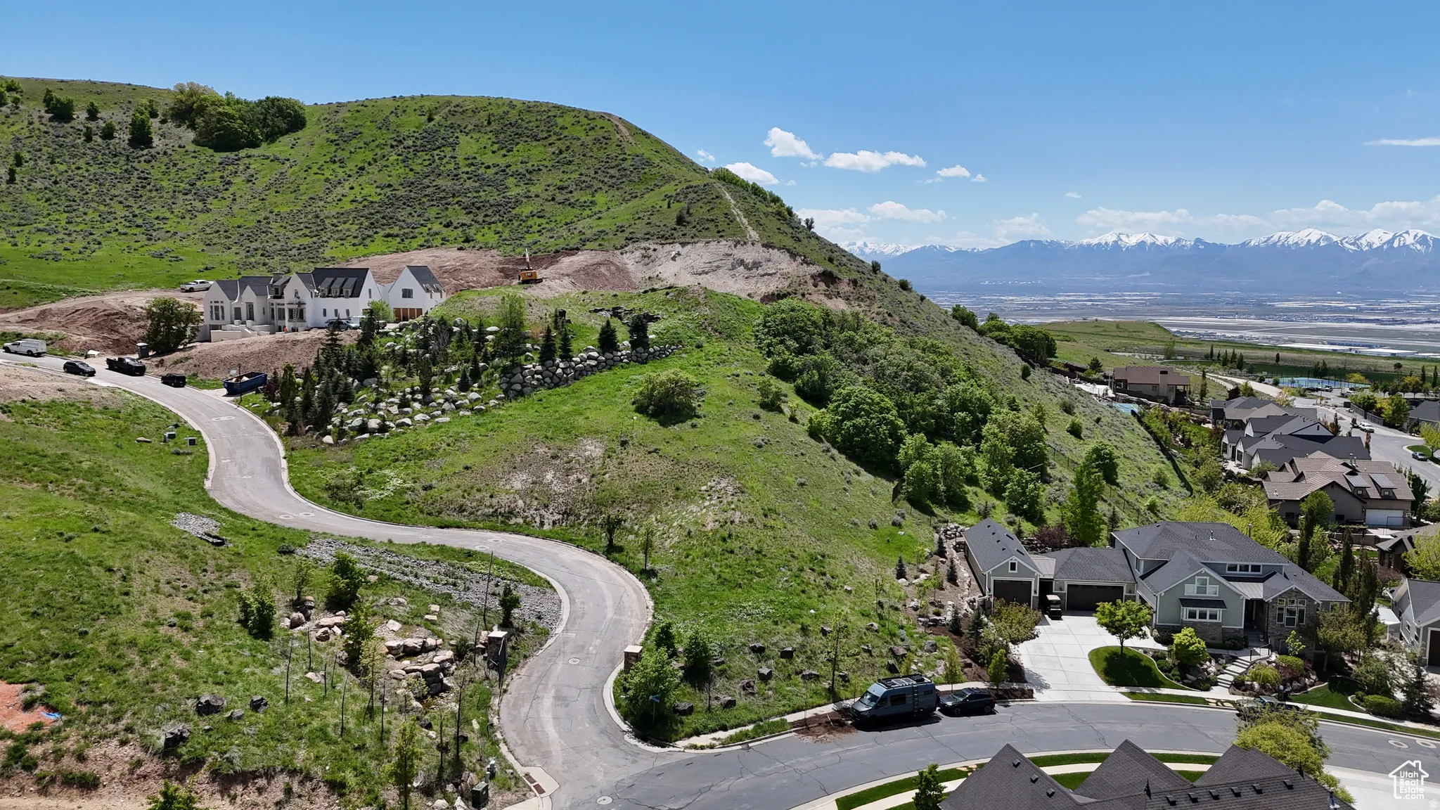 Winding roadway ascending a green hillside with residential properties