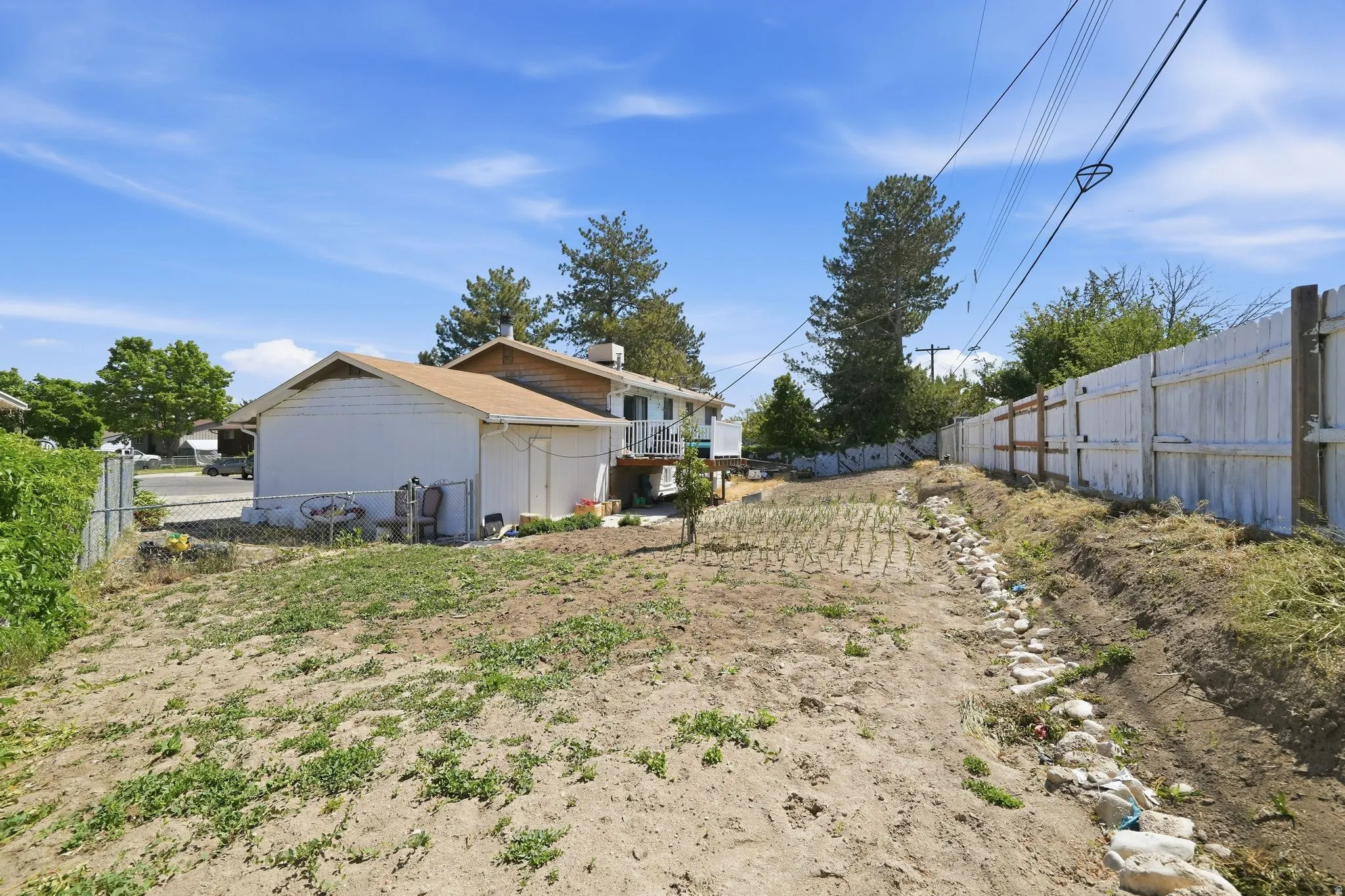Expansive outdoor area featuring a planted garden bed, a wooden privacy fence, and a detached structure