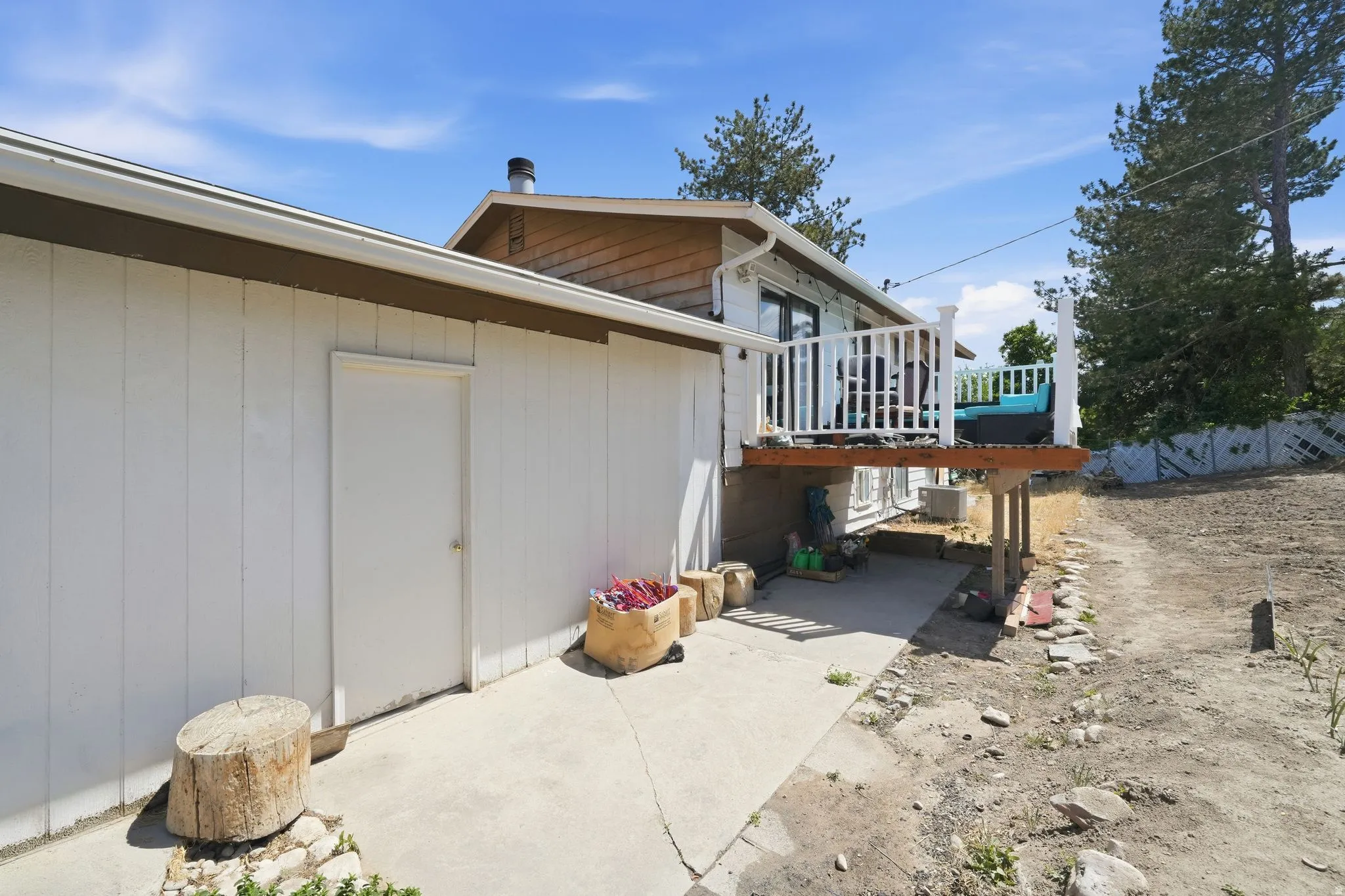 Exterior featuring a white paneled facade, upper-level wood deck with white railings, and a concrete patio below