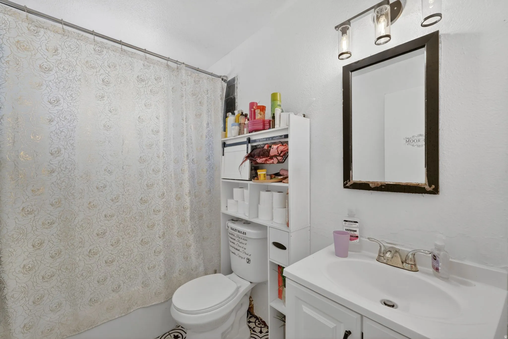 Bathroom featuring a white vanity with an integrated sink, polished chrome faucet, and a wall-mounted mirror with an overhead three-light fixture