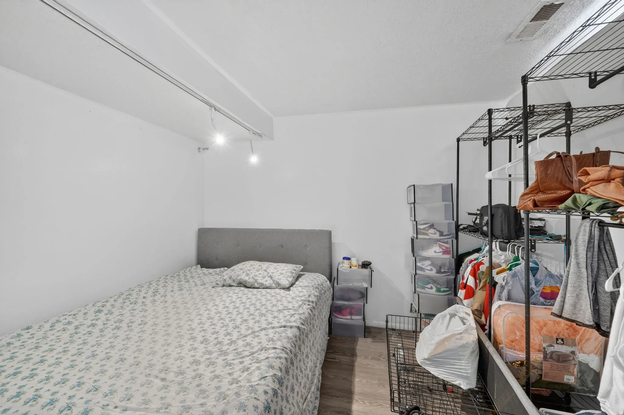 Room featuring track lighting, a gray upholstered headboard, and wood-finish flooring