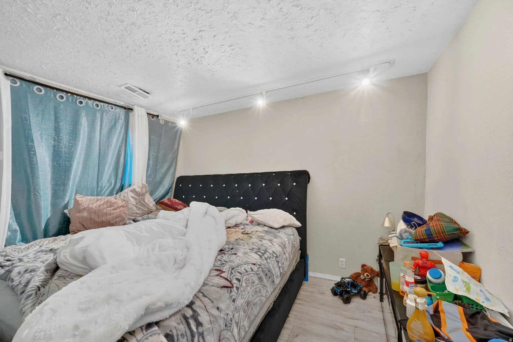 Bedroom featuring light neutral wall paint, overhead track lighting, and wood-finish flooring