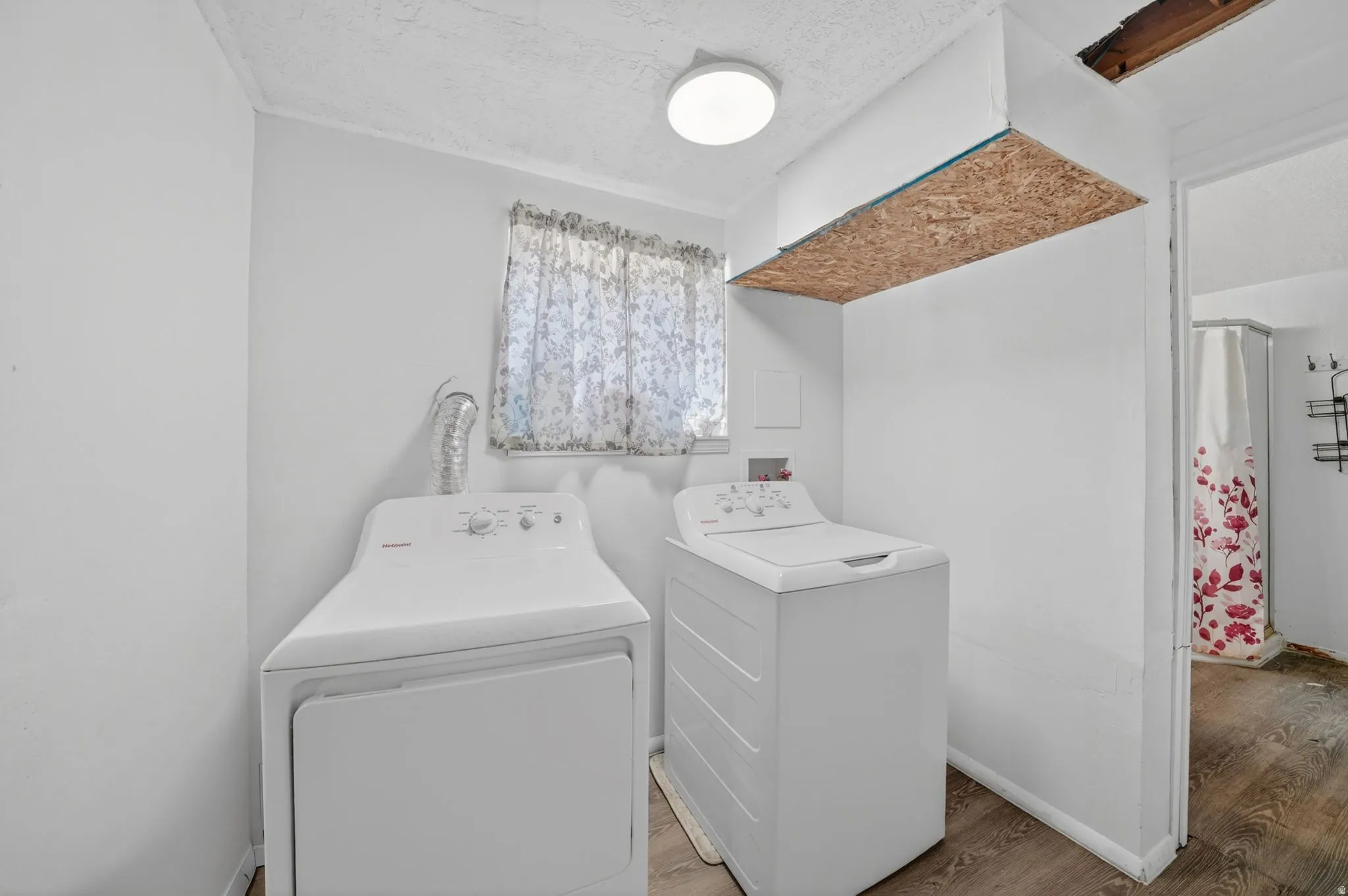 Laundry area featuring a window with patterned curtains, a ceiling-mounted light fixture, and wood-finish flooring