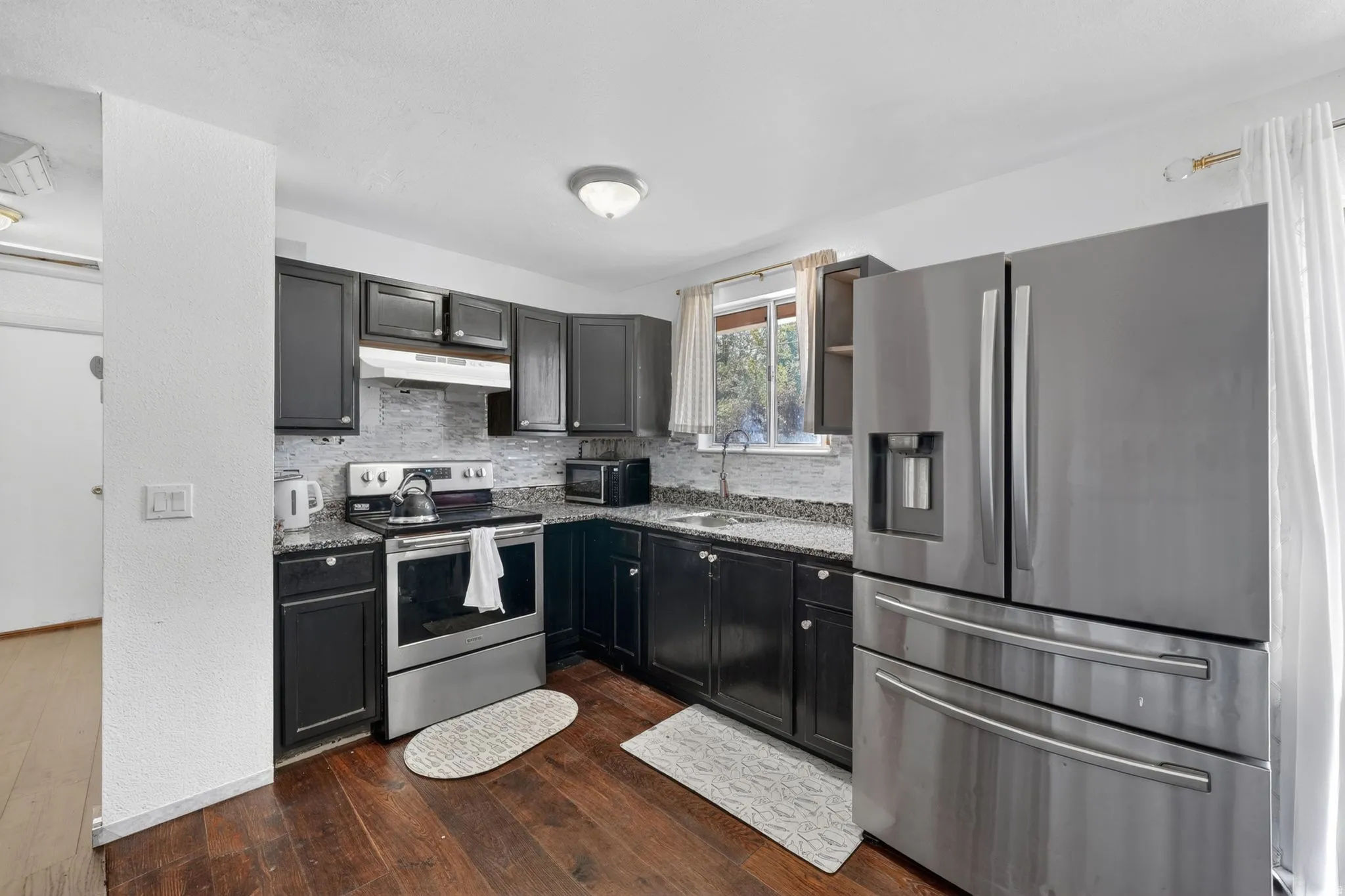 Kitchen featuring dark wood-finish cabinetry, speckled countertops, stainless steel appliances, and wood-finish flooring