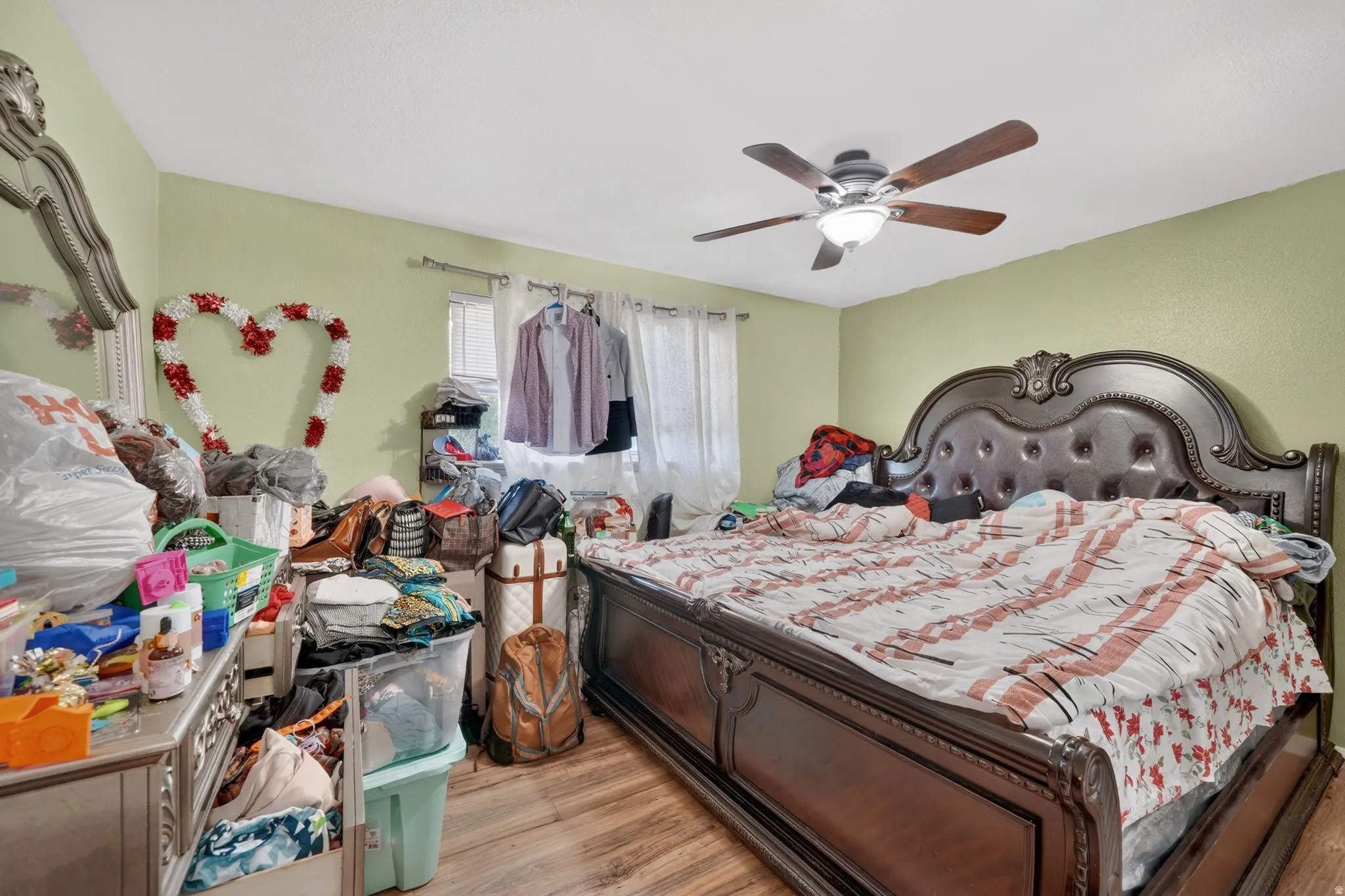 Bedroom featuring wood-finish flooring, light green walls, a ceiling fan with integrated lighting, and a window with blinds