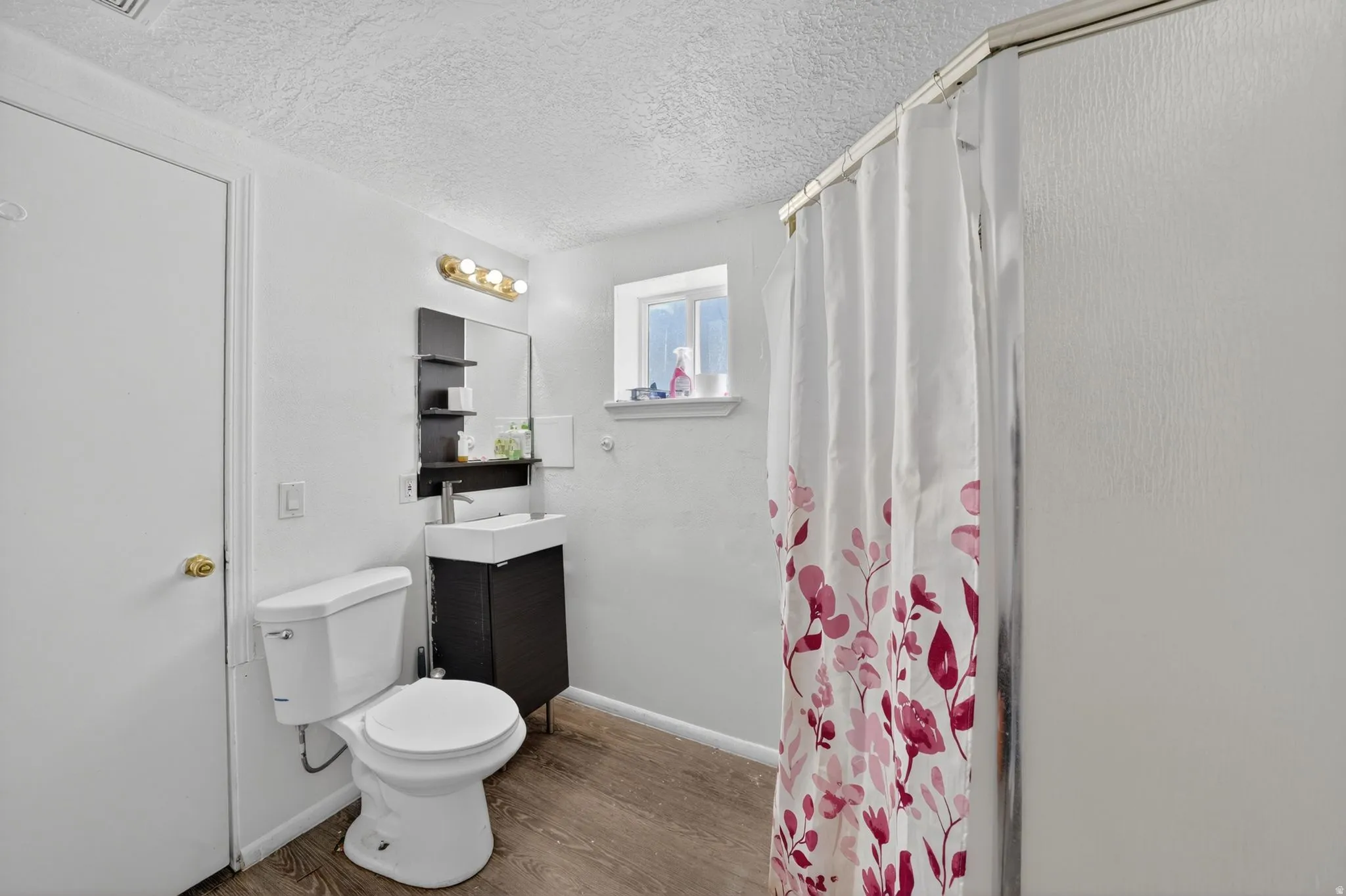 Bathroom featuring a white toilet, dark wood-finish vanity with a rectangular basin sink, and a shower with a sliding enclosure