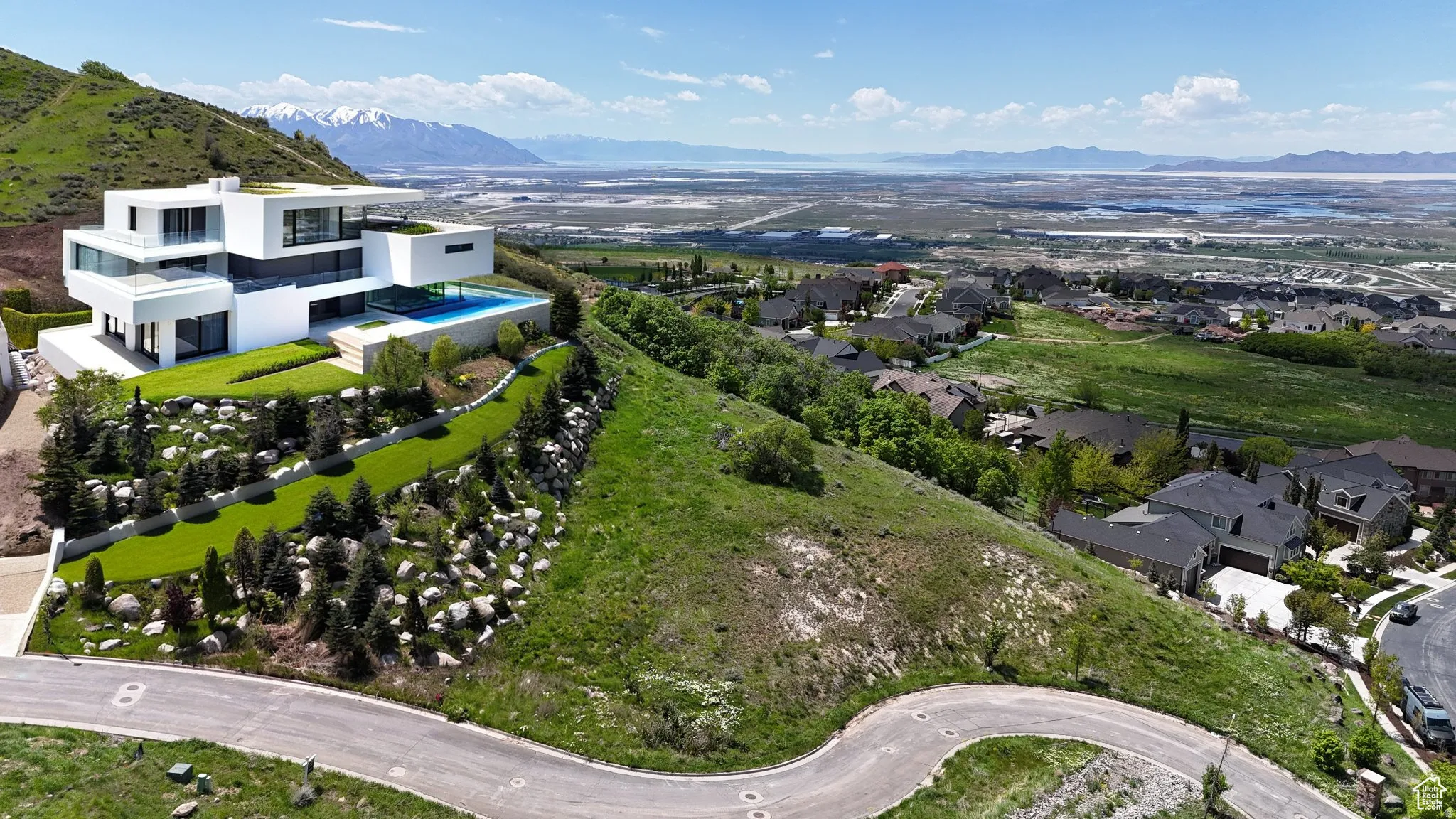 Contemporary multi-level residence featuring expansive windows, an infinity-edge pool, and a tiered landscaped yard with mature plantings and rock formations