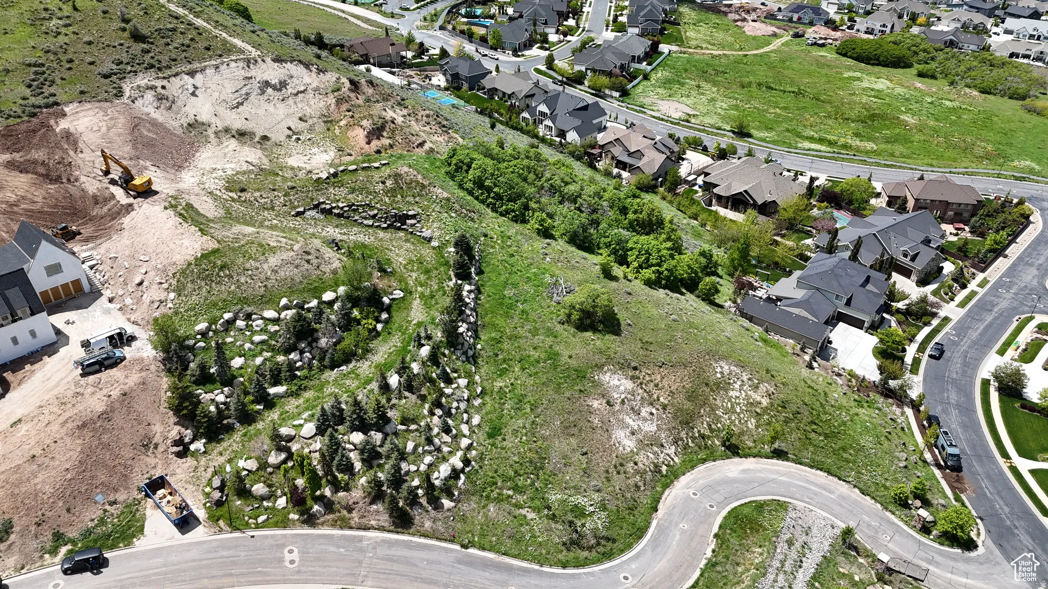 Spacious sloped lot featuring natural rock formations, scattered evergreen trees, and surrounding residential properties