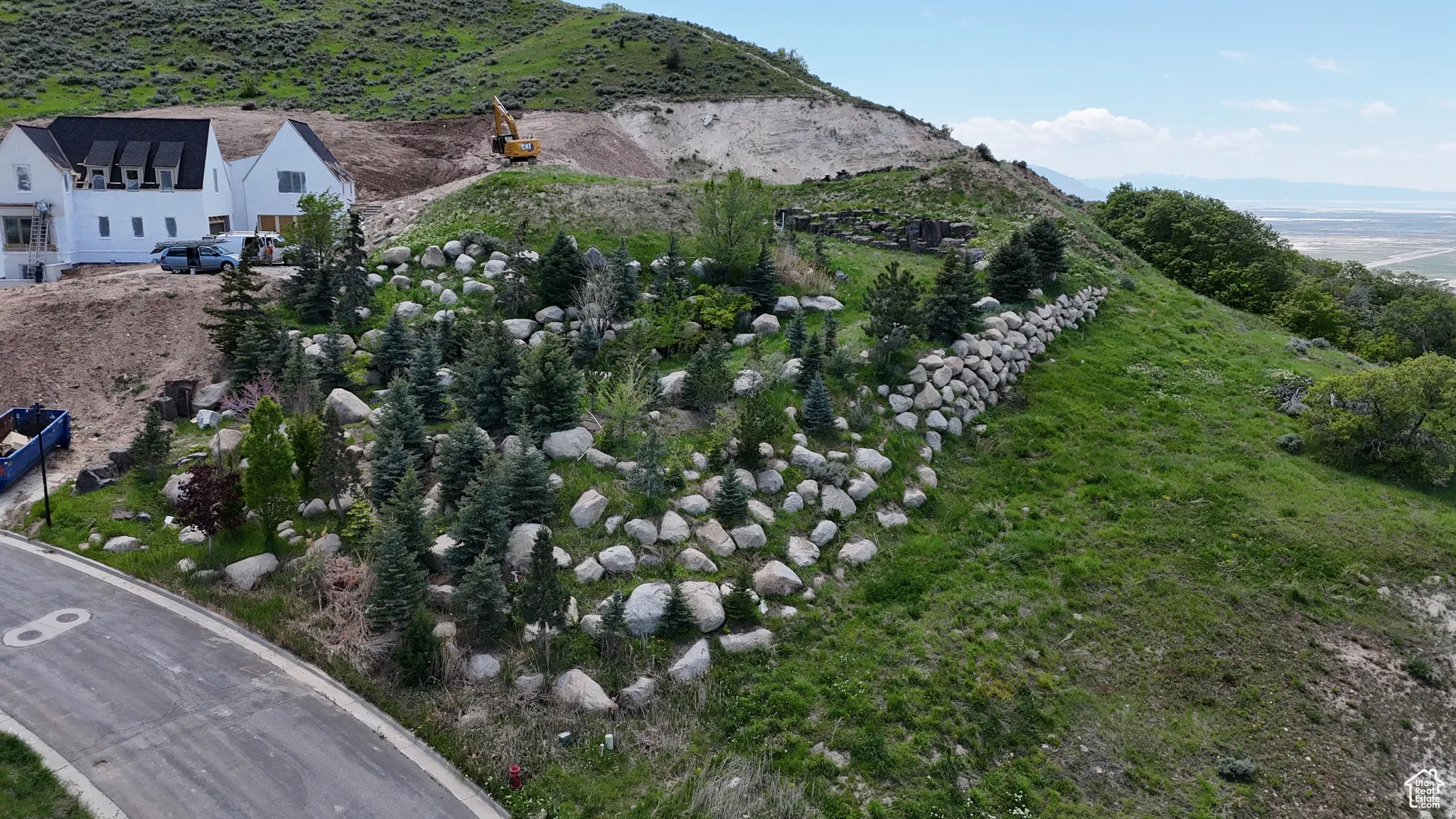 Sloping hillside property featuring a white exterior residence under construction with dormer windows and dark roofing
