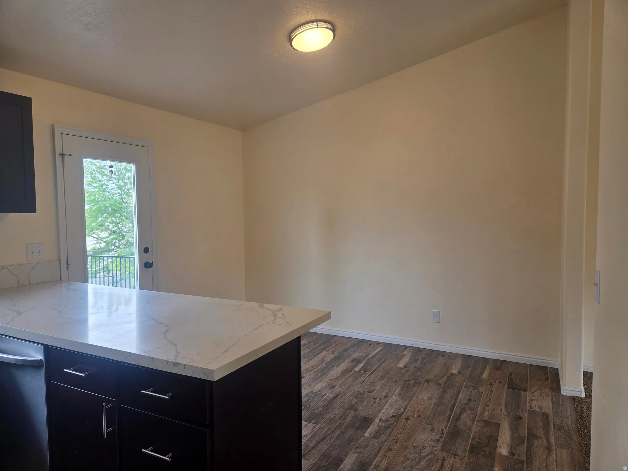 Kitchen area featuring a white quartz countertop island with dark wood cabinetry and chrome hardware, wood-finish flooring, and a glass-paneled door leading to an exterior balcony with a black railing