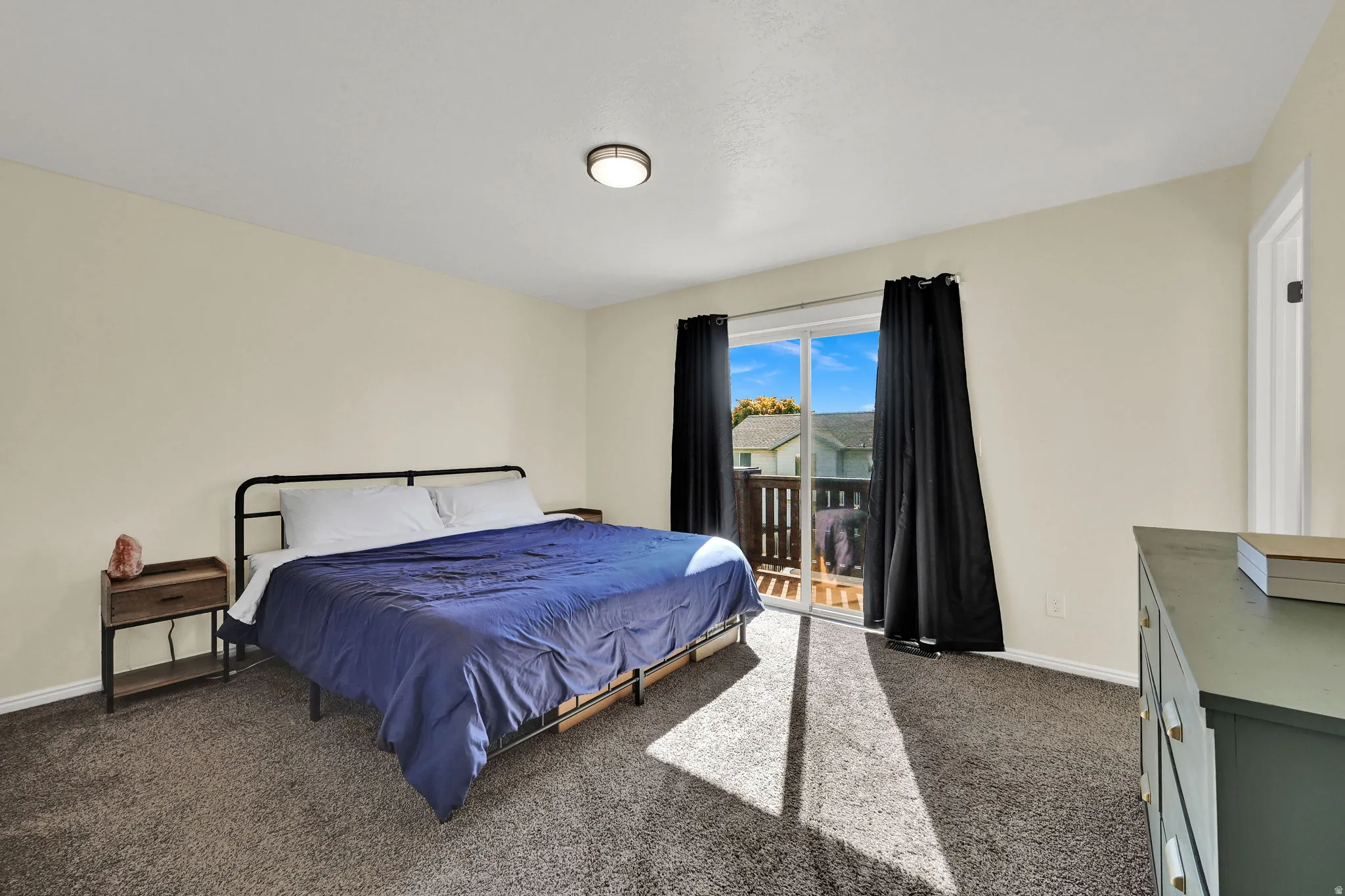 Bedroom featuring neutral tone walls, dark gray carpeting, and a sliding glass door leading to an exterior deck with wood railings