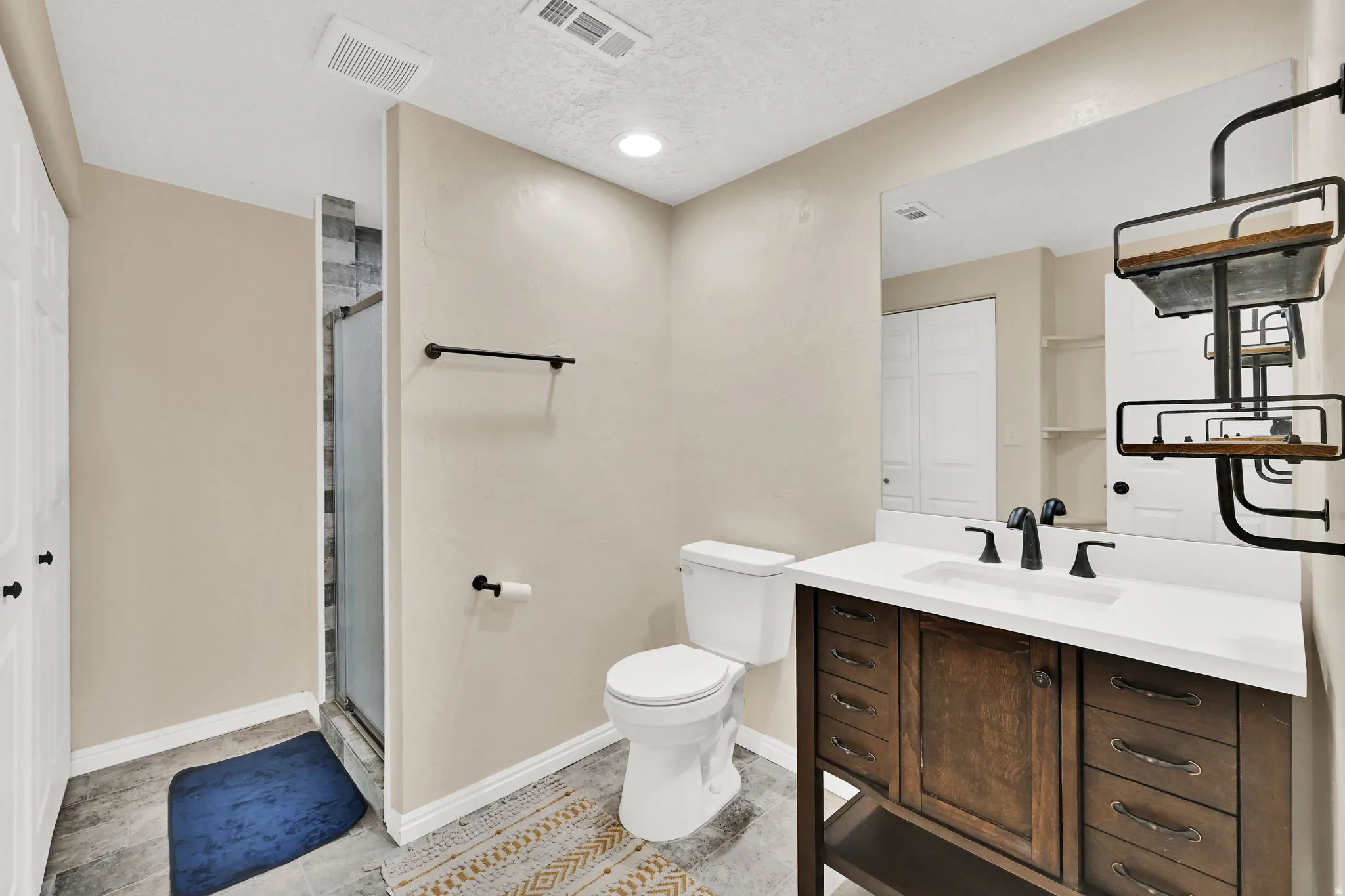 Bathroom featuring a dark wood-finish vanity with a white countertop and integrated sink, a glass-enclosed shower with gray tiled walls, and white paneled doors