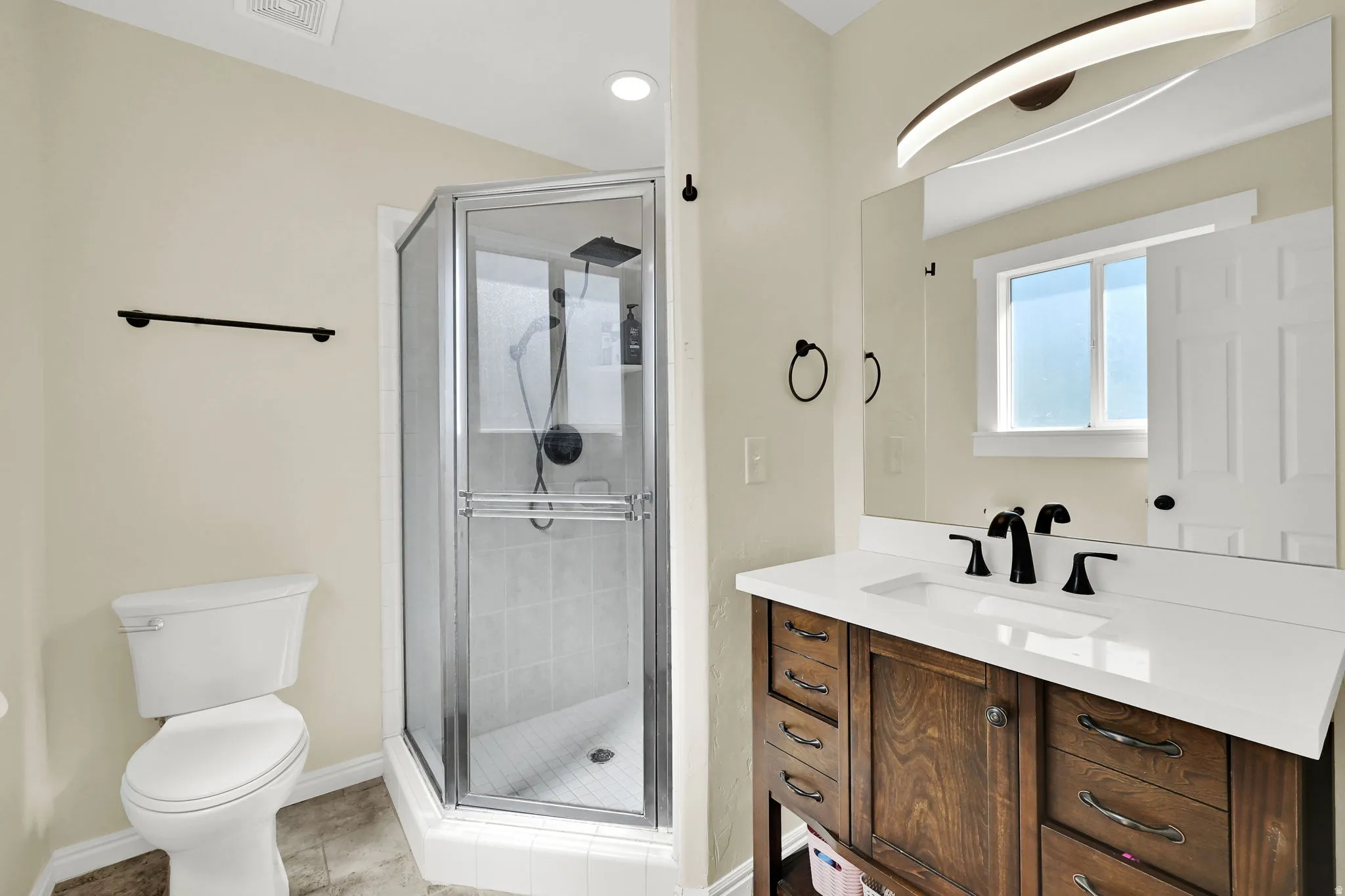 Bathroom featuring a wood-finish vanity with a white countertop, inset sink, and matte black fixtures