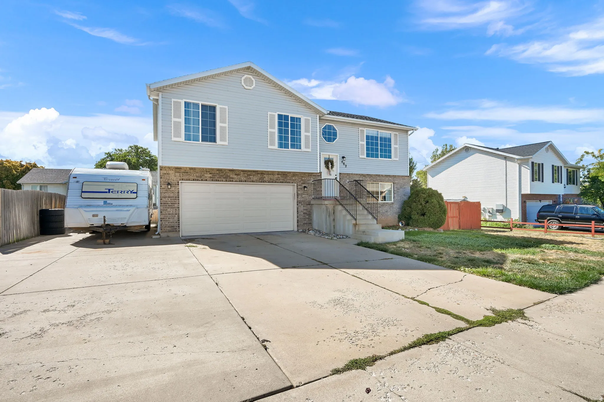 Split-level residence featuring light blue siding with white trim, stone veneer accents, an attached two-car garage, concrete driveway, and white window shutters